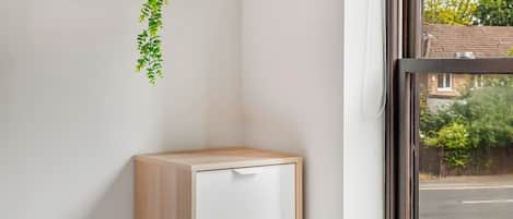 A corner of a room with a white cabinet, a hanging plant, and a window with a view of a street and trees.