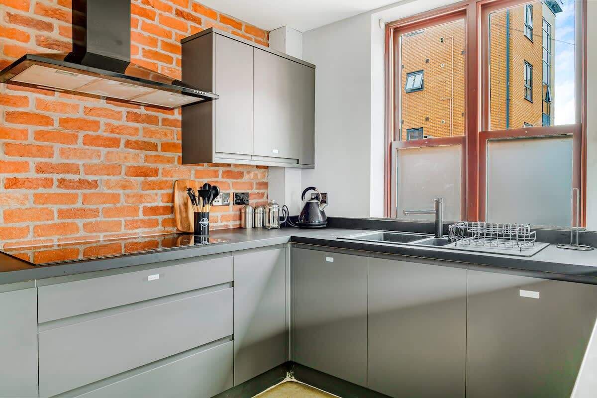A modern kitchen with a brick wall, stainless steel cabinets, a black countertop, and a window with a view of a brick building.