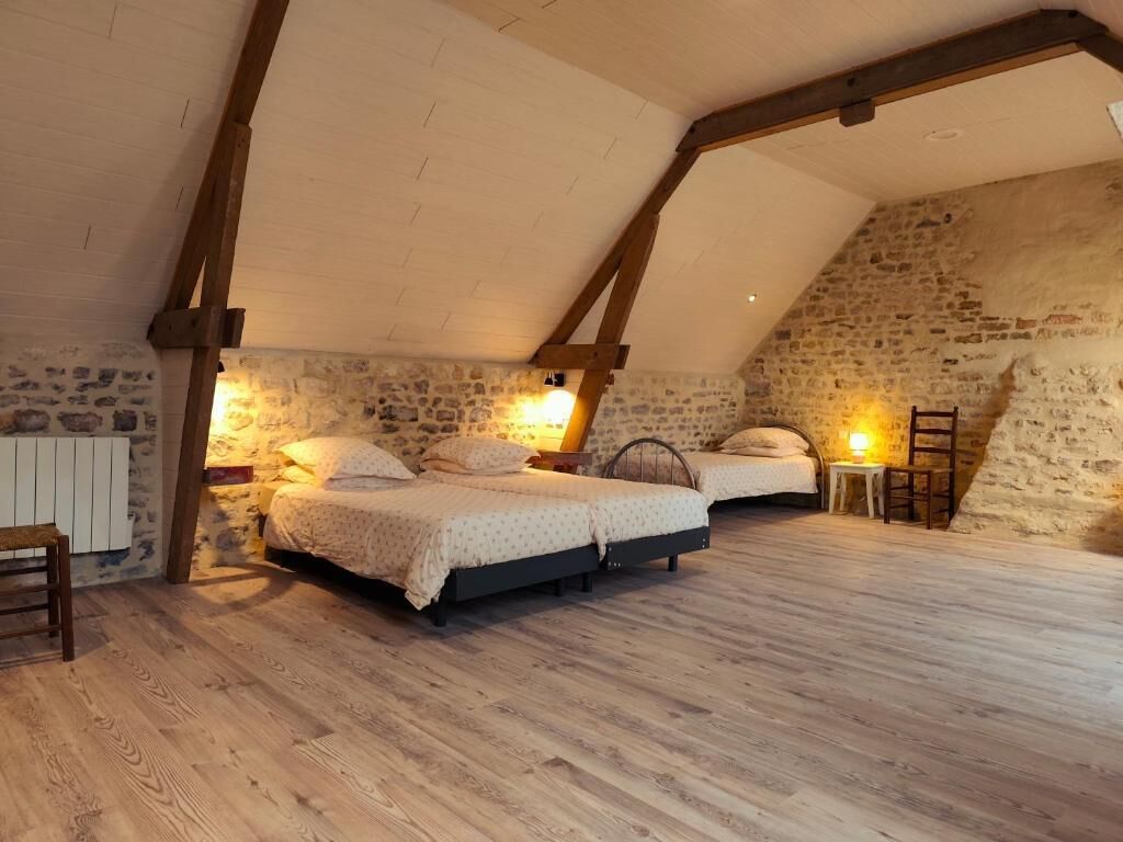 Une chambre avec deux lits, des murs en pierre, des poutres en bois et un plafond en pente.