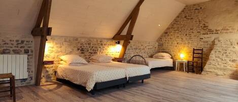 A bedroom with two beds, stone walls, wooden beams, and a sloped ceiling.
