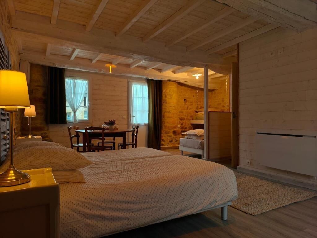 A bedroom with a bed, bedside table, lamp, and a view of a dining area.