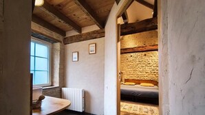 Een smalle gang die leidt naar een slaapkamer met een stenen muur, een bed en een raam.