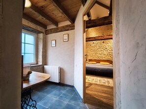 A narrow hallway leading to a bedroom with a stone wall, a bed, and a window.