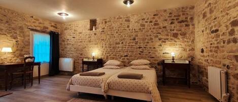 Une chambre avec un mur en pierre, un lit double, des tables de chevet avec des lampes, un bureau avec une chaise et un radiateur.