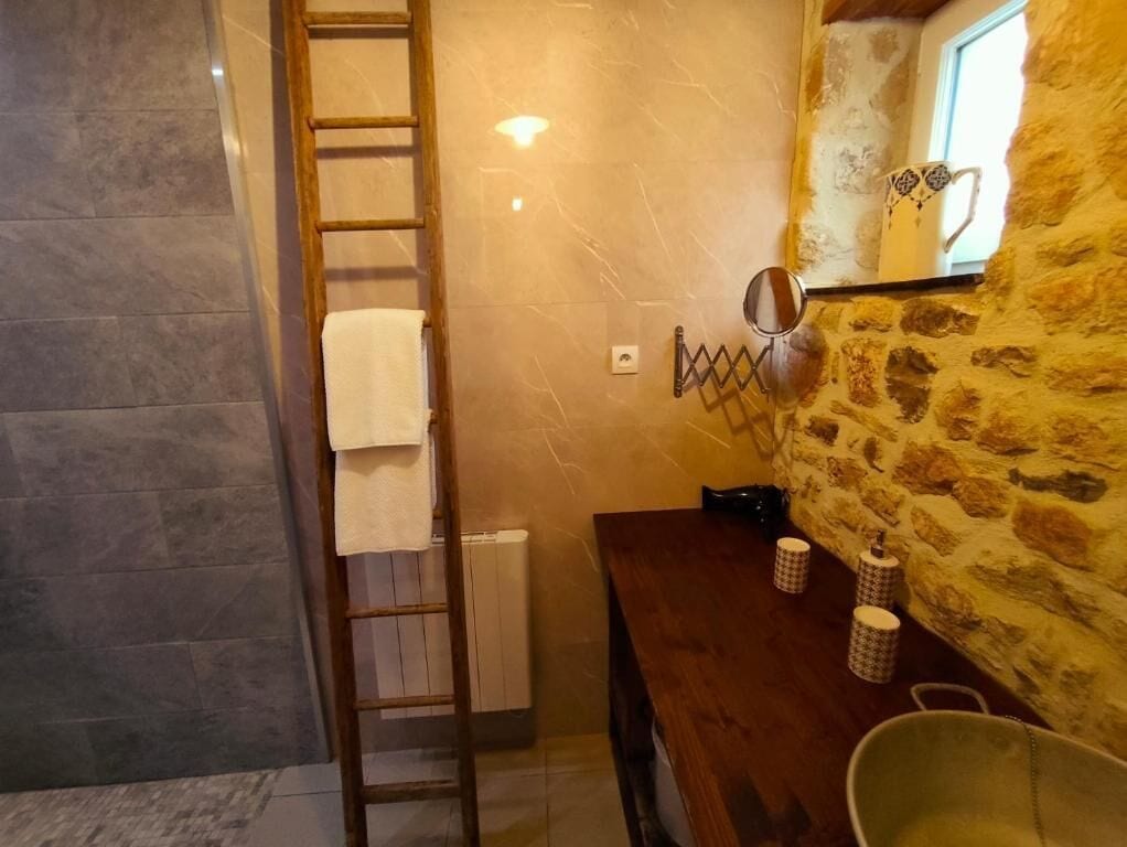 A bathroom with a wooden ladder, a towel rack, a stone wall, and a window with a decorative mug.