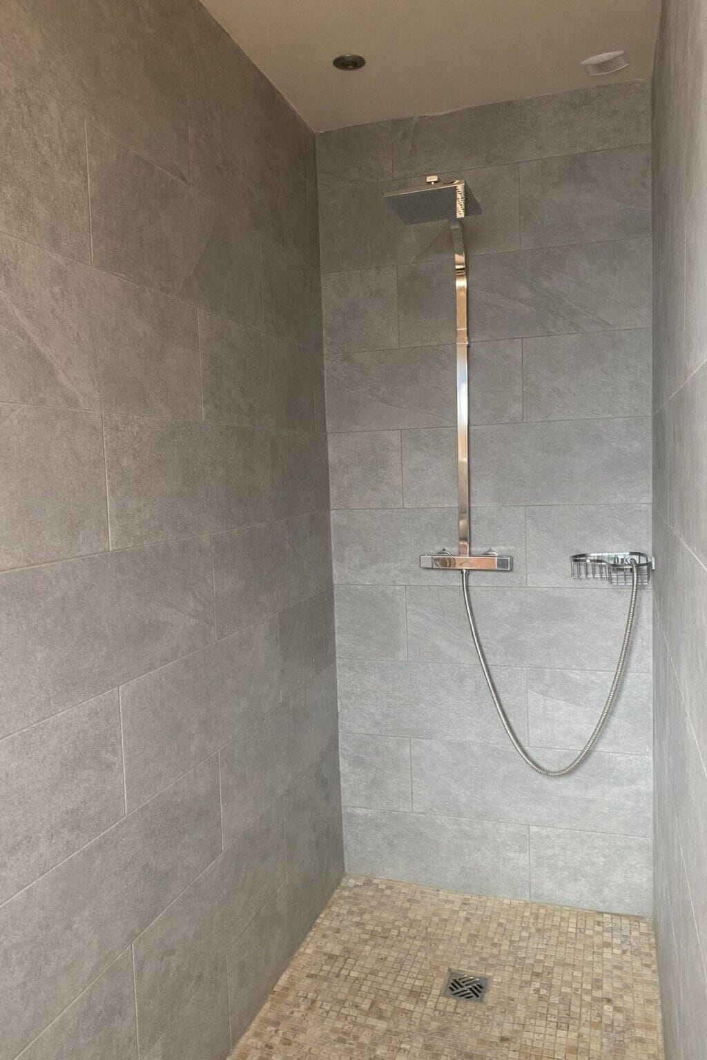 A shower with a handheld showerhead and a wall-mounted faucet.
