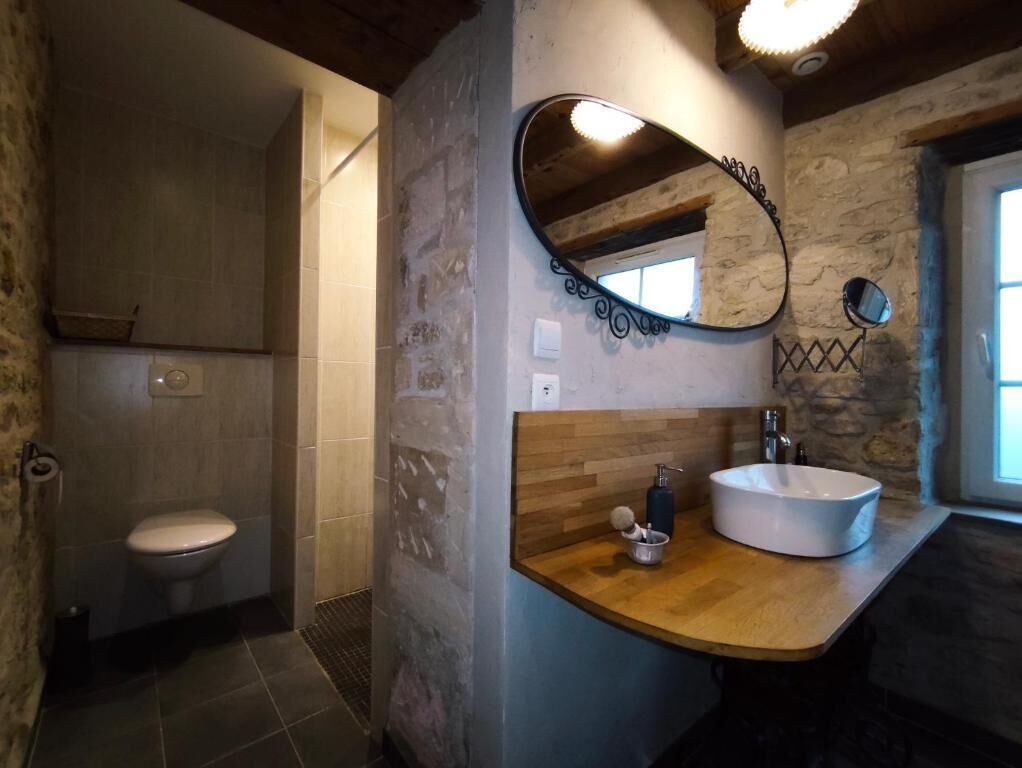 Une salle de bain avec un mur en pierre, un meuble-lavabo en bois, un lavabo blanc et un miroir.