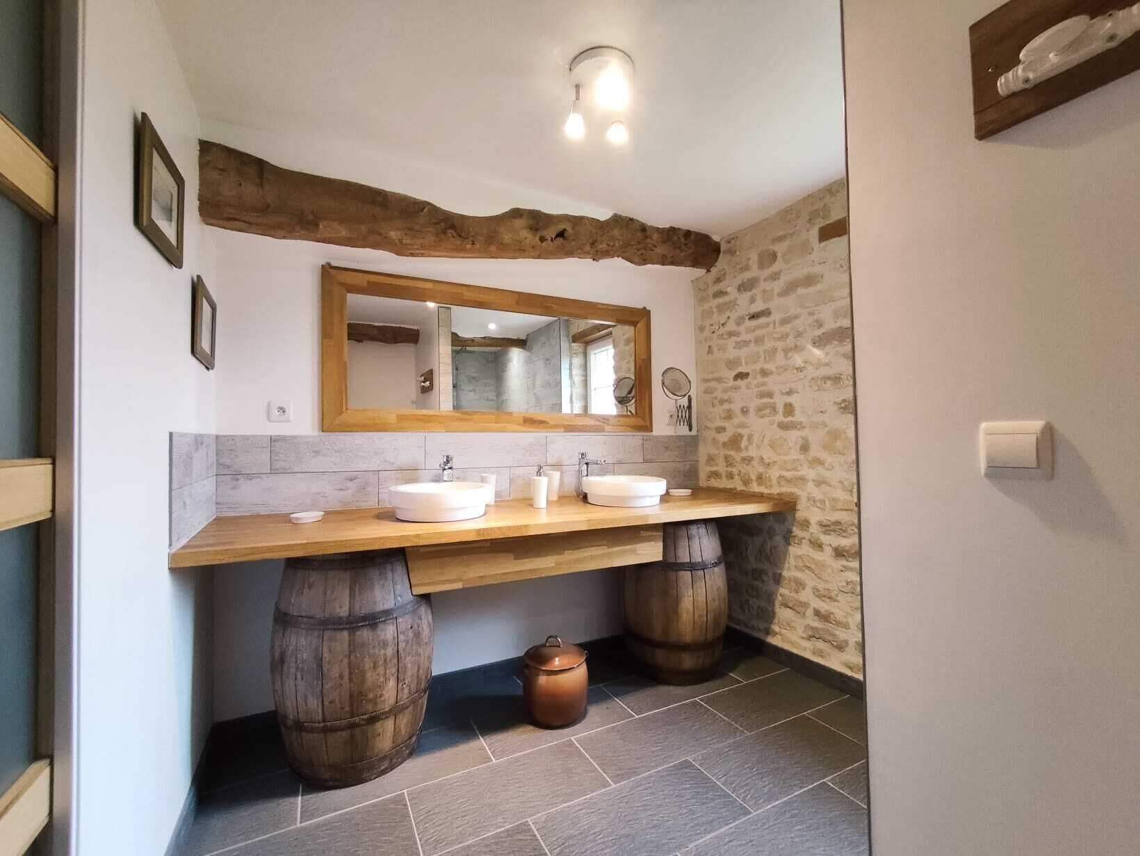 Een badkamer met een rustieke inrichting, met een houten wastafelmeubel met twee wastafels, een grote spiegel en stenen muren.