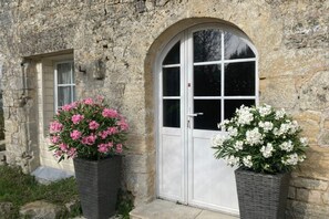 A stone building with a white door and two flower planters, one with pink flowers and the other with white flowers.
