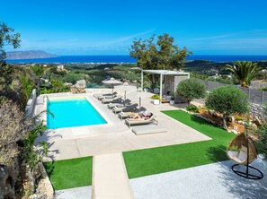 A pool area with lounge chairs and a pergola, surrounded by greenery and a view of the sea. - Dream Vacation Home with Ocean View, Private Pool, and Garden in Kournas (Kournas Natures Nest)