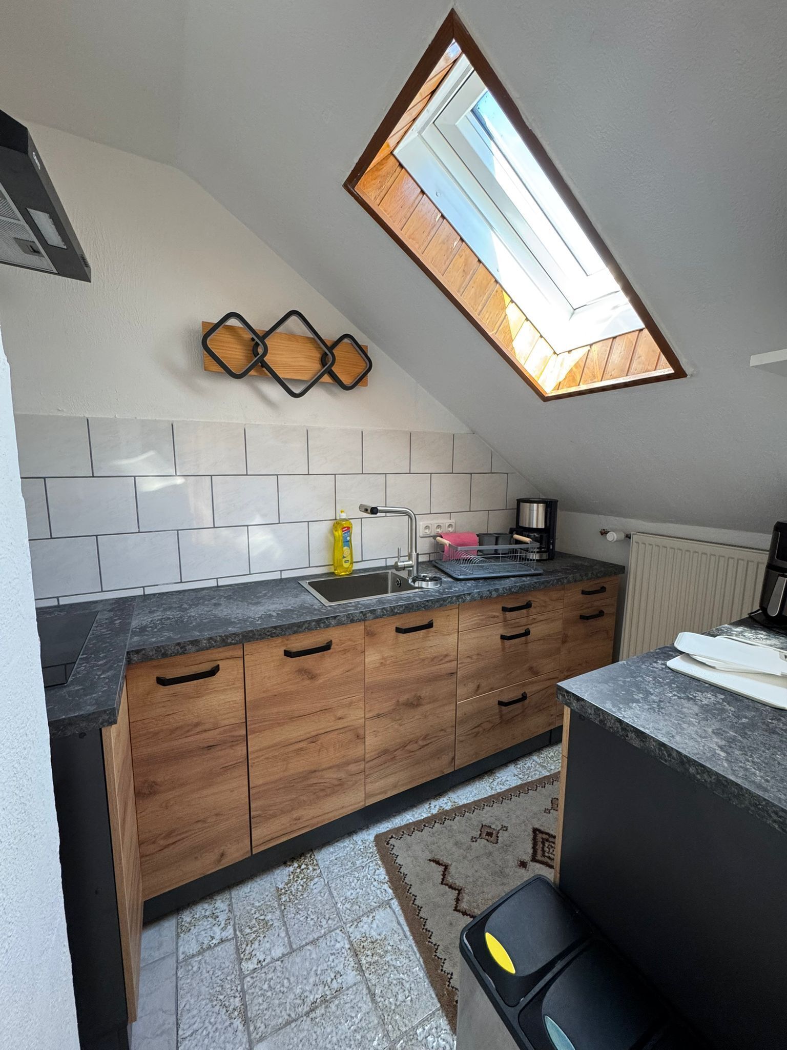 Eine Küche mit Oberlicht, Holzschränken, einer Granitarbeitsplatte und einem gemusterten Teppich.