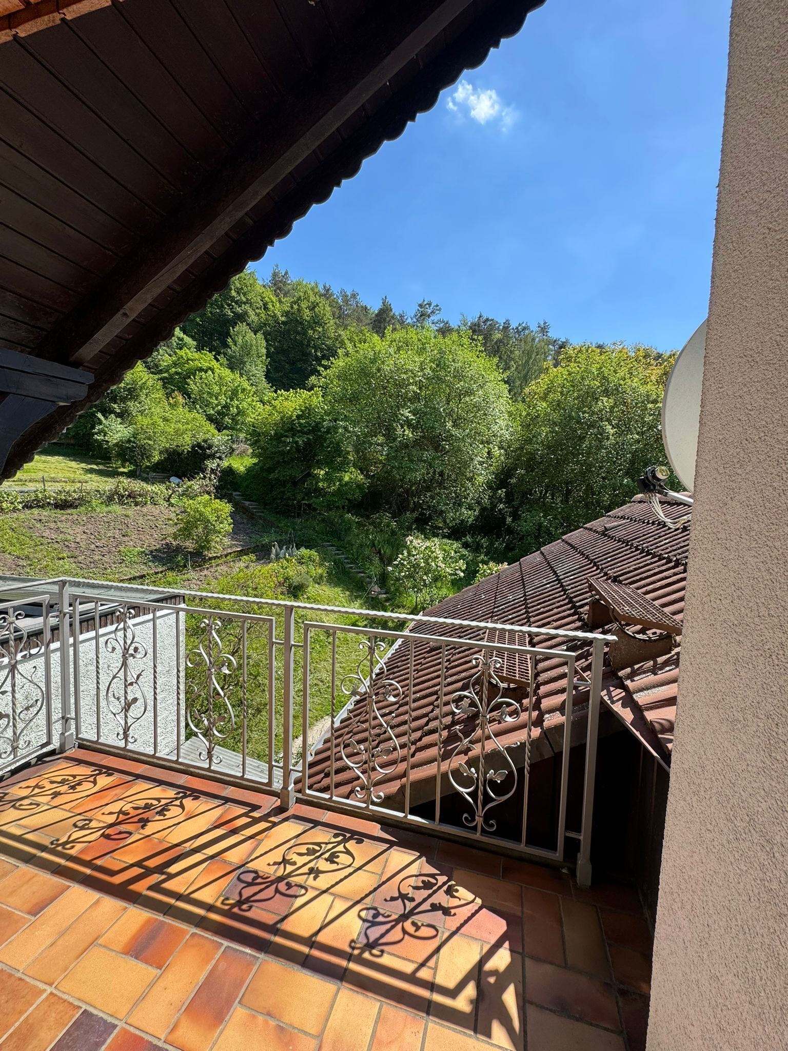 Ein Balkon mit Fliesenboden, Metallgeländer und Blick auf einen bewaldeten Hügel.