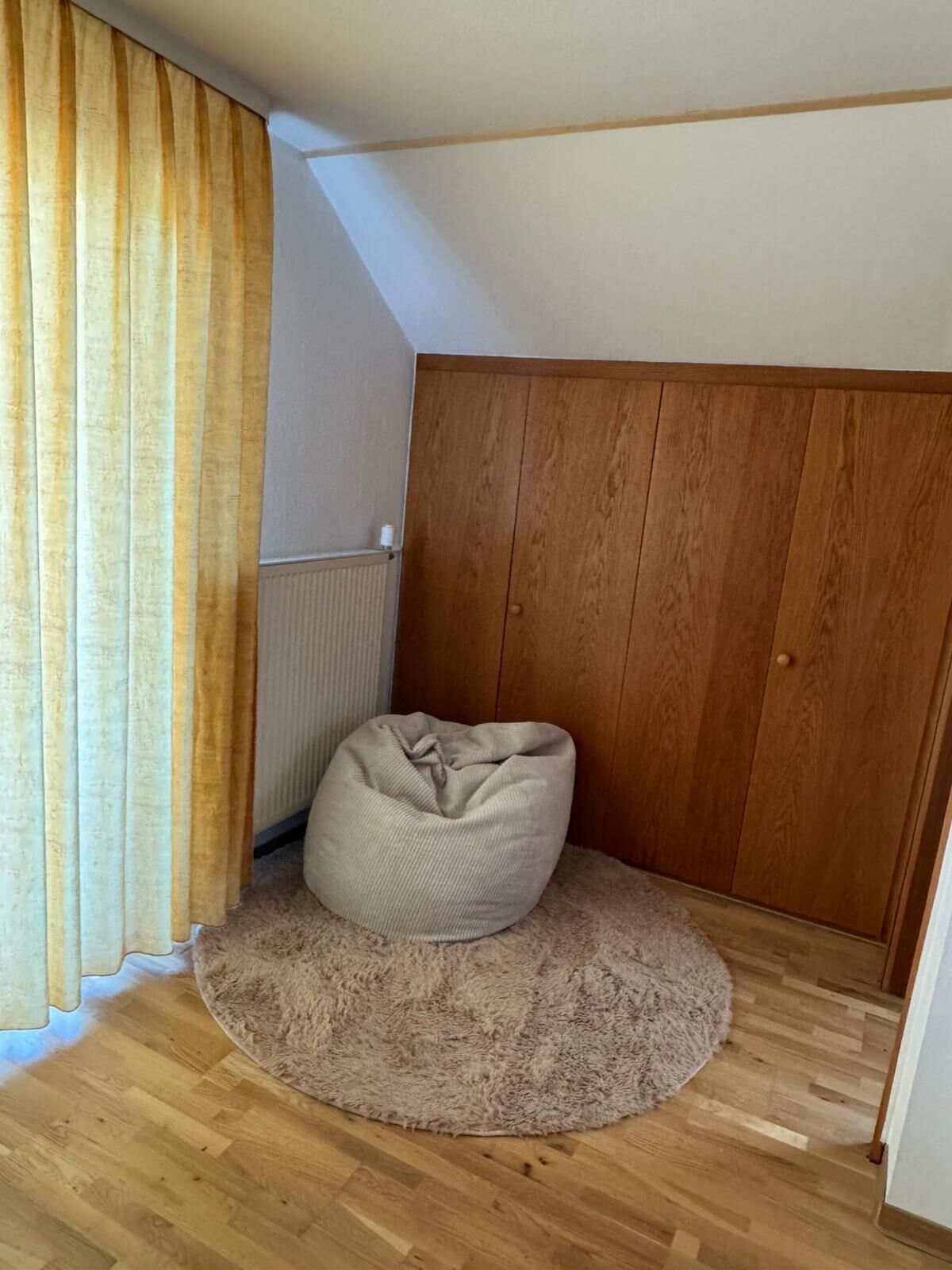 Ein Zimmer mit einem Holzschrank, einem beige farbenen Sitzsack und einem flauschigen Teppich auf Holzböden.