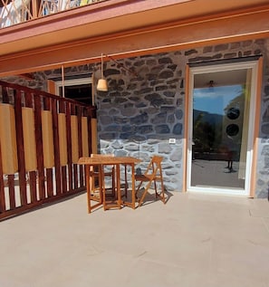 Eine Terrasse mit Steinmauer, Holztisch und -stühlen sowie einer Glastür zu einem Außenbereich.
