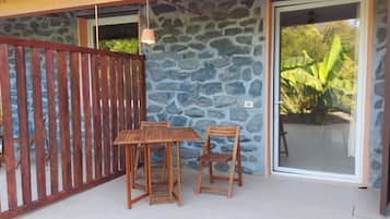 Eine Terrasse mit Holztisch und Stühlen, einer Steinmauer und einer Glastür, die in einen Garten führt.