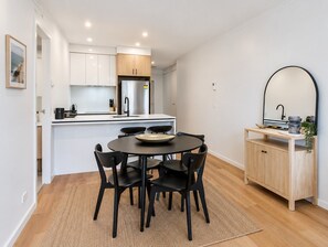 A modern kitchen with white cabinets, a black dining table with chairs, and a wooden cabinet with a mirror. - Apt 2 - 18 Remembrance Drive - Surfers Paradise (Surfers Paradise)