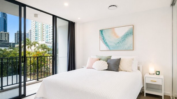 Una camera da letto con un letto grande, un comodino, un quadro e un balcone con vista sulla città.