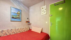 Habitació amb un llit, una porta verda, un quadre al mur i una petita estant amb objectes.