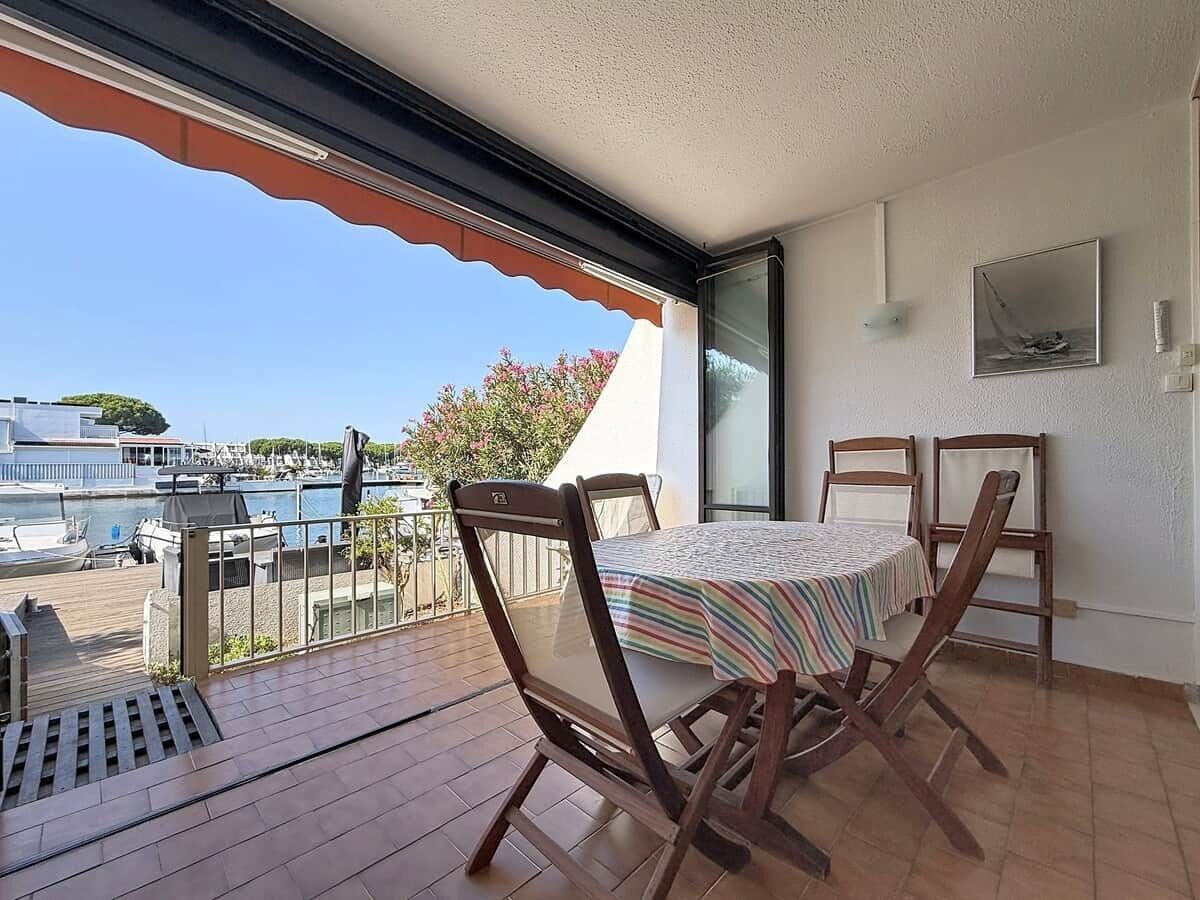 Un balcon avec une table et des chaises, une vue sur un port de plaisance et un immeuble à la façade blanche.