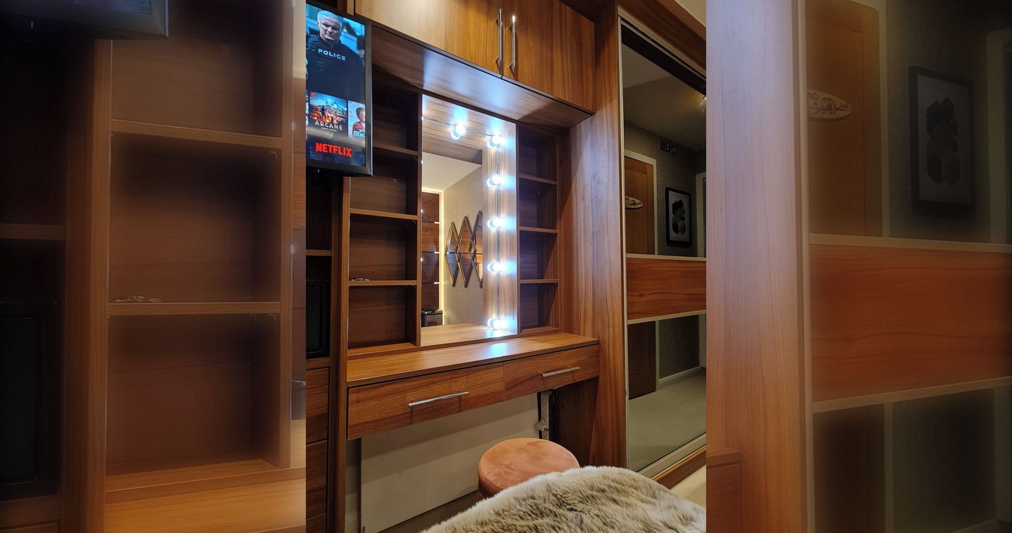 A walk-in closet with wooden shelving, a vanity with a mirror, and a television displaying a movie.