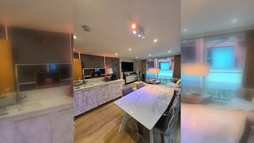 A modern kitchen with marble countertops, a dining area with a large table, and a living space with a TV and large windows.