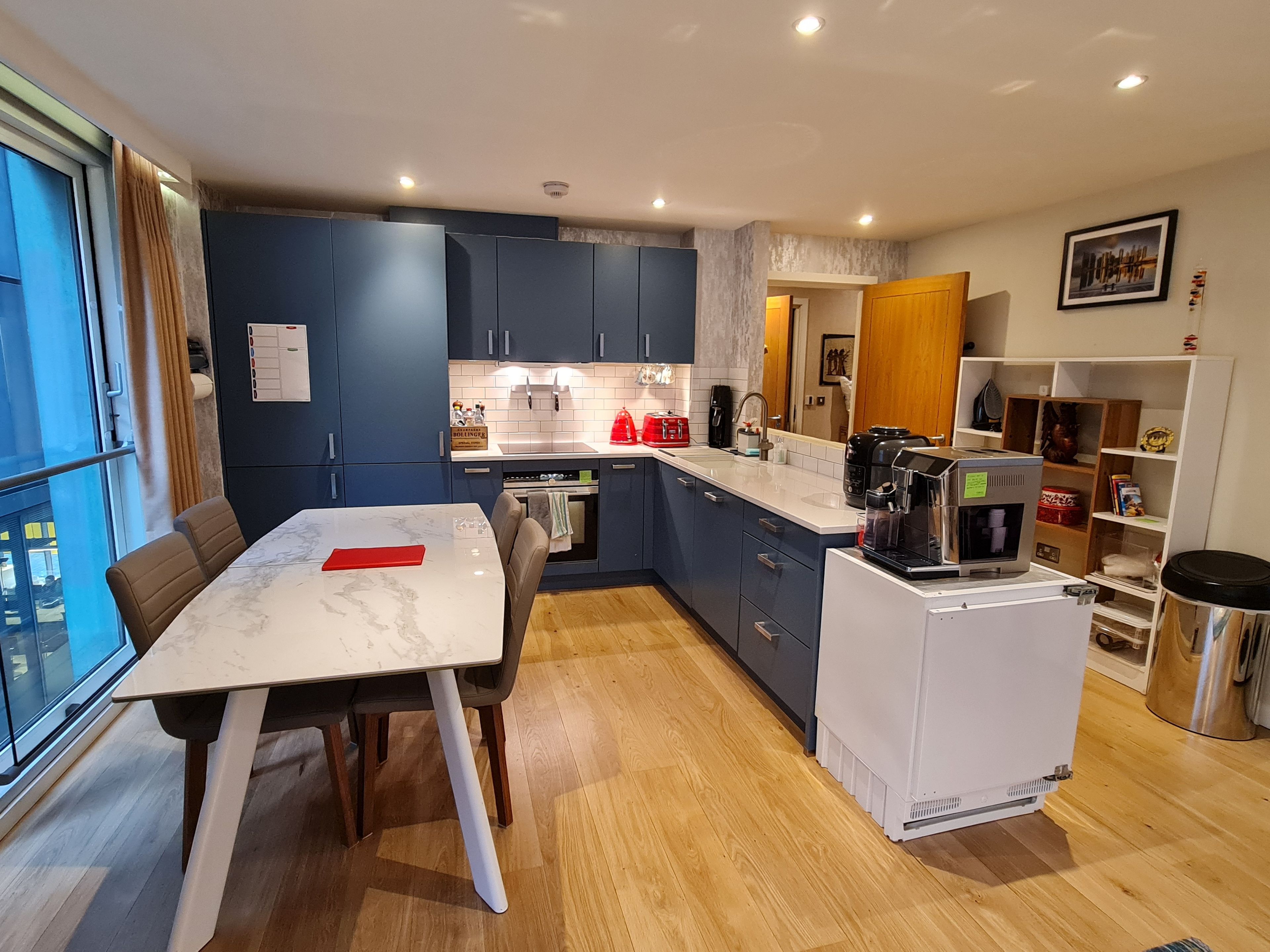A modern kitchen with blue cabinets, a white countertop, and a dining area with a marble table.