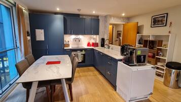 A modern kitchen with blue cabinets, a white countertop, and a dining area with a marble table.