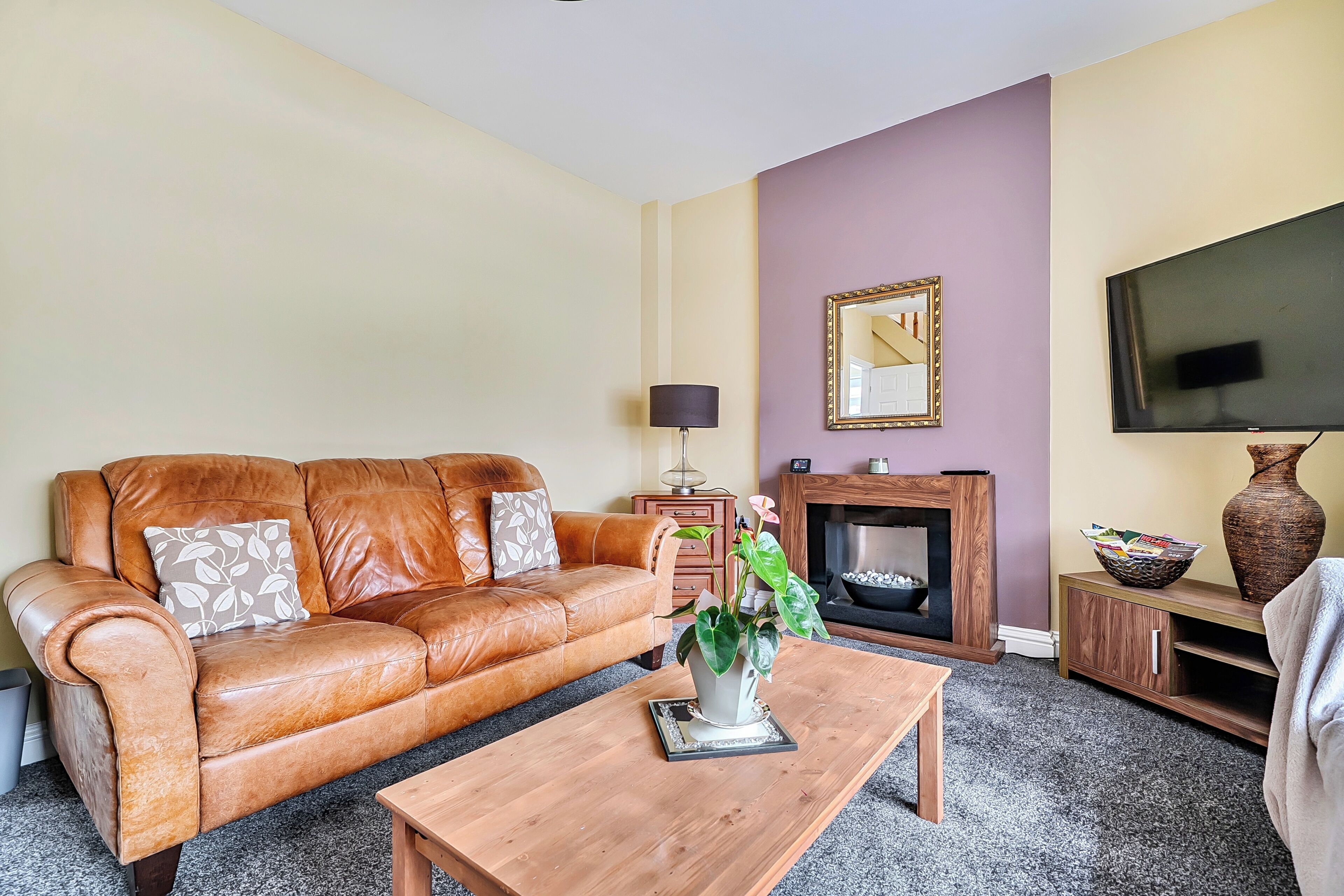 A living room with a leather sofa, a coffee table, a fireplace, and a television.
