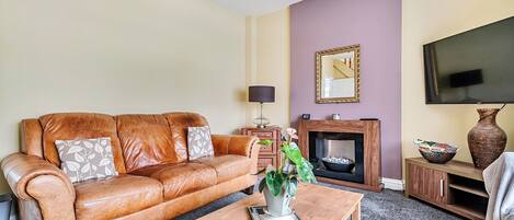A living room with a leather sofa, a coffee table, a fireplace, and a television.