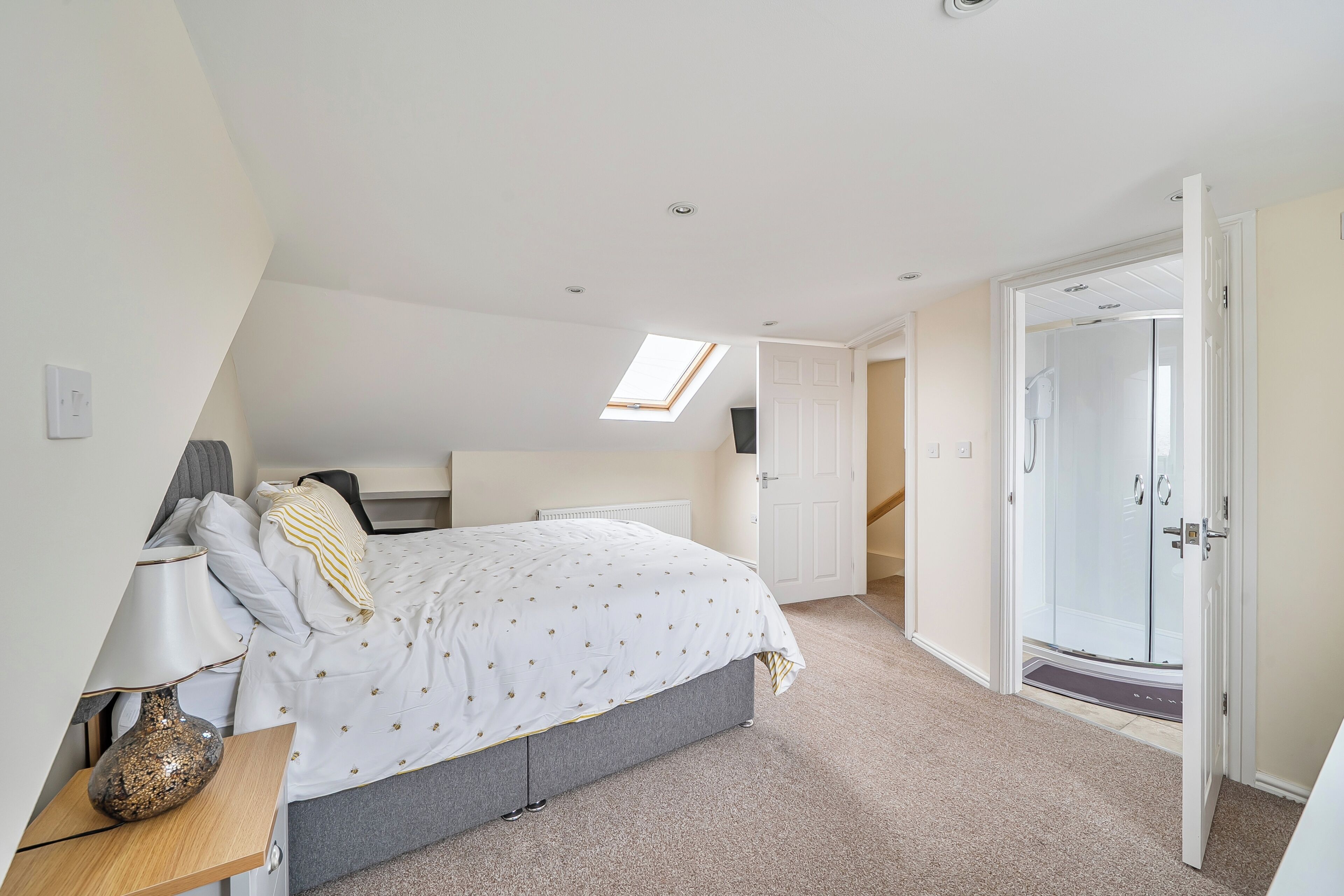 A bedroom with a bed, bedside table, lamp, and a skylight.