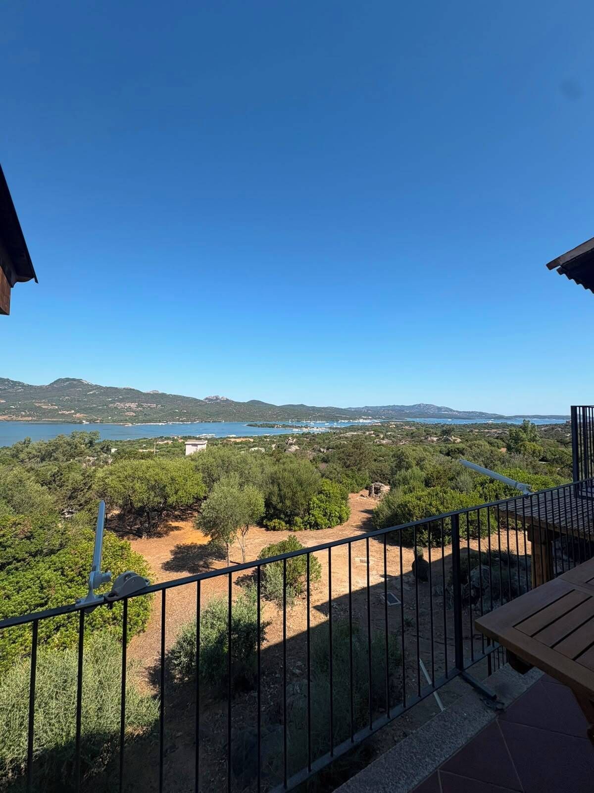 Ein Balkon mit Blick auf eine Küstenlandschaft, darunter ein Gewässer und ferne Hügel.