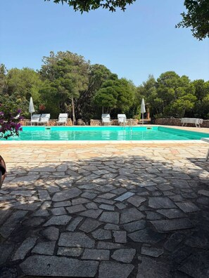 A swimming pool with lounge chairs and umbrellas, surrounded by stone tiles and trees. - Porto Rotondo Costa Smeralda Sea-view apartment, residence with pool, tennis (Porto Rotondo)