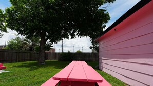 Una mesa de picnic roja en un patio trasero con una cerca de madera y una casa al fondo.