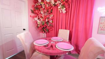 A dining area with a glass table, pink chairs, and a floral backdrop.