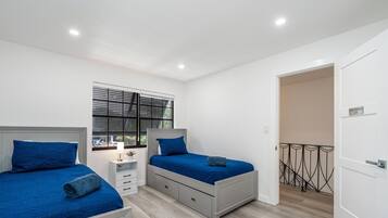 Un dormitorio con dos camas, una ventana con persianas, una mesita de noche y una puerta a un balcón.