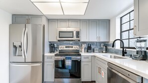 A modern kitchen with stainless steel appliances, grey cabinets, a dishwasher, and a large window. - Fox Palace Pool House (Fort Lauderdale)