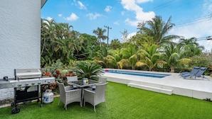 A backyard with a grill, outdoor furniture, a swimming pool, and lush greenery. - Fox Palace Pool House (Fort Lauderdale)