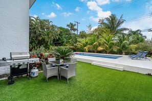 Ein Garten mit Grill, Gartenmöbeln, einem Swimmingpool und üppigem Grün.