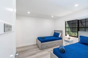 A bedroom with two beds, a window with blinds, a bedside table with a lamp, and a sign indicating the room is a 'CHRISTENSEN SUITE.'
