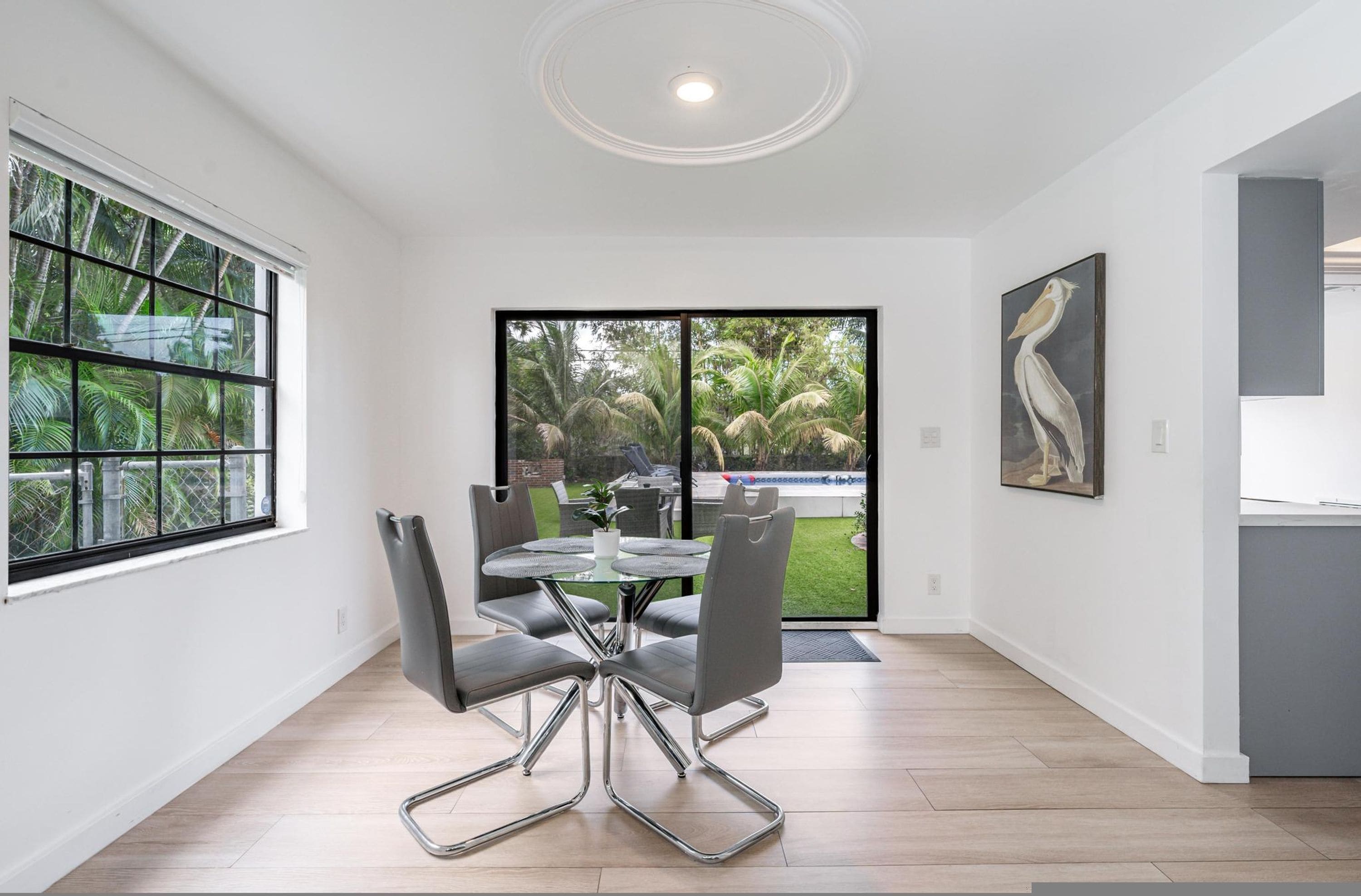Un comedor moderno con una mesa de vidrio, sillas metálicas y vista a un jardín a través de puertas de cristal.