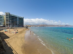 Ein Strand mit klarem, blauem Wasser, einem sandigen Ufer und einem modernen Mehrstöckiger Gebäude.
