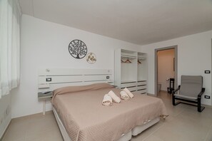 A bedroom with a bed, a chair, a wardrobe, and a mirror. - Domo Archea (Olbia)