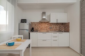 Une cuisine compacte avec des meubles blancs, un four à micro-ondes, une machine à café et un dosseret carrelé.