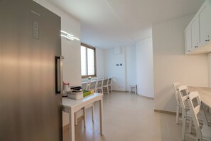A modern kitchen with white cabinetry, a built-in oven, and a dining area with a table and chairs. - Domo Archea (Olbia)