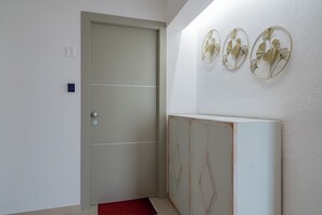 A hallway with a door, a wall-mounted light fixture, and a red doormat. - Domo Archea (Olbia)