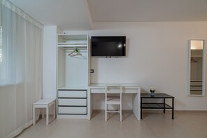 Une chambre moderne et minimaliste, avec un bureau blanc, un téléviseur fixé au mur, une petite table sur laquelle est posée une plante en pot et une armoire avec un espace pour suspendre des vêtements.