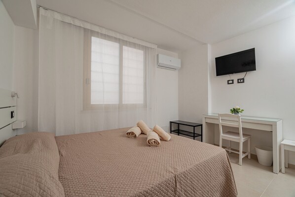 A hotel room with a bed, a desk, a chair, a TV, and an air conditioning unit. - Domo Archea (Olbia)