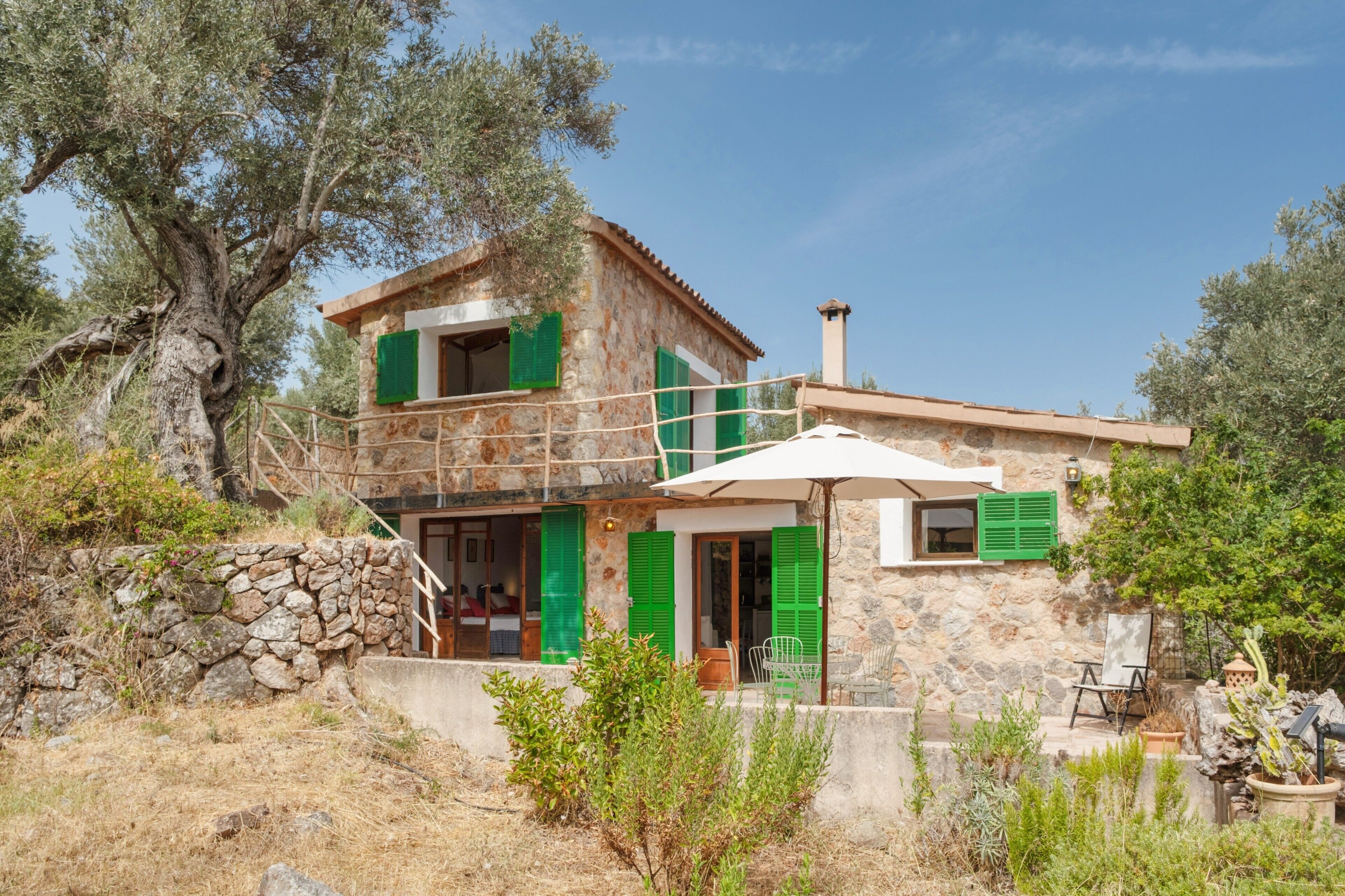 A stone house with green shutters, a balcony, and a cactus plant.