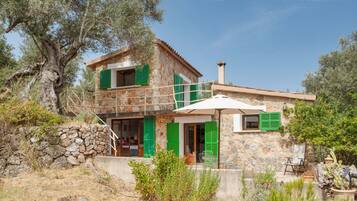 Une maison en pierre avec des volets verts, un balcon et un cactus.