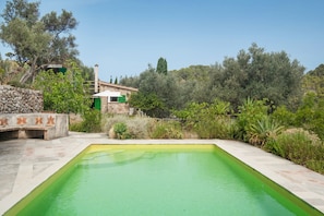 A rectangular swimming pool with a stone border, surrounded by greenery and a stone wall with decorative tiles. - Holiday Home 'Can Carabá' with Mountain Views, Private Pool, and Wi-Fi (Sóller)